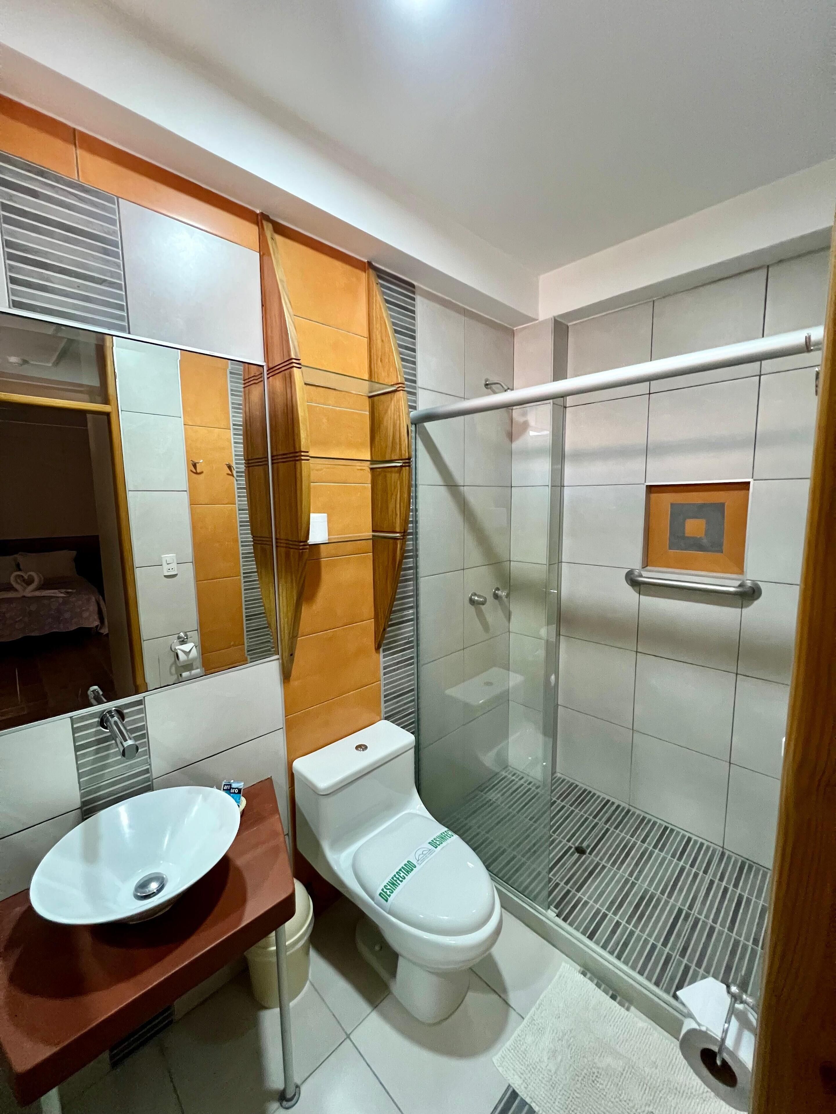 Et moderne badeværelse med brusekabine i glas, en hvid vask og et toilet.