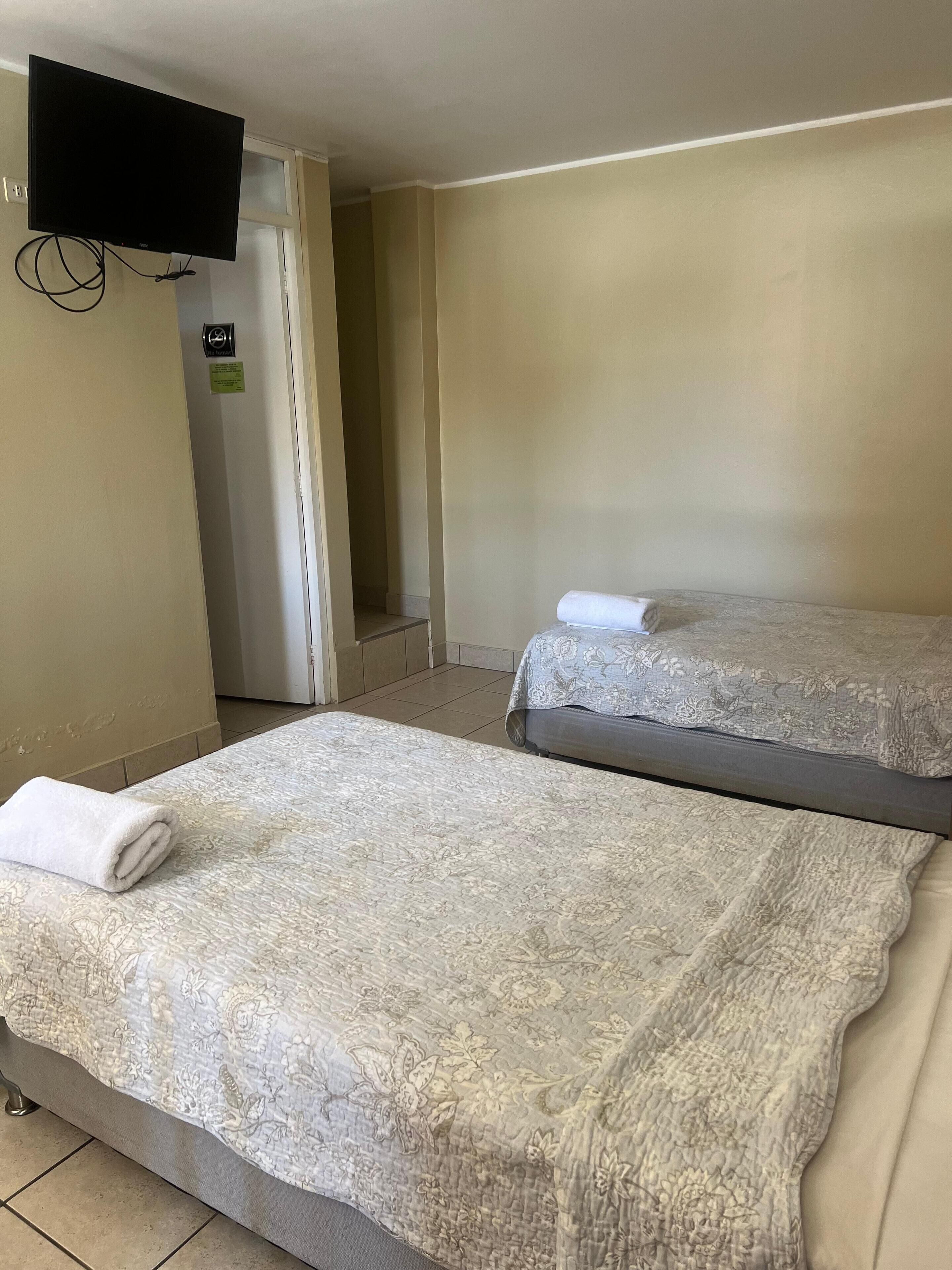 Een hotelkamer met twee bedden, een flatscreen televisie aan de muur en een deur naar een gang.