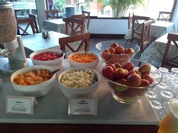Un bufé de desayuno con diversas frutas y una máquina de café.