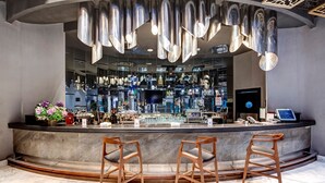 Eine Bar mit einer gebogenen Theke, Holzbarhocker und einem modernen Kronleuchter.