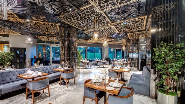 Ein modernes Restaurant mit hoher Decke, verziert mit aufwendigen Mustern, Marmorböden und einer Mischung aus Sitzgelegenheiten, darunter Tische und eine Couch.