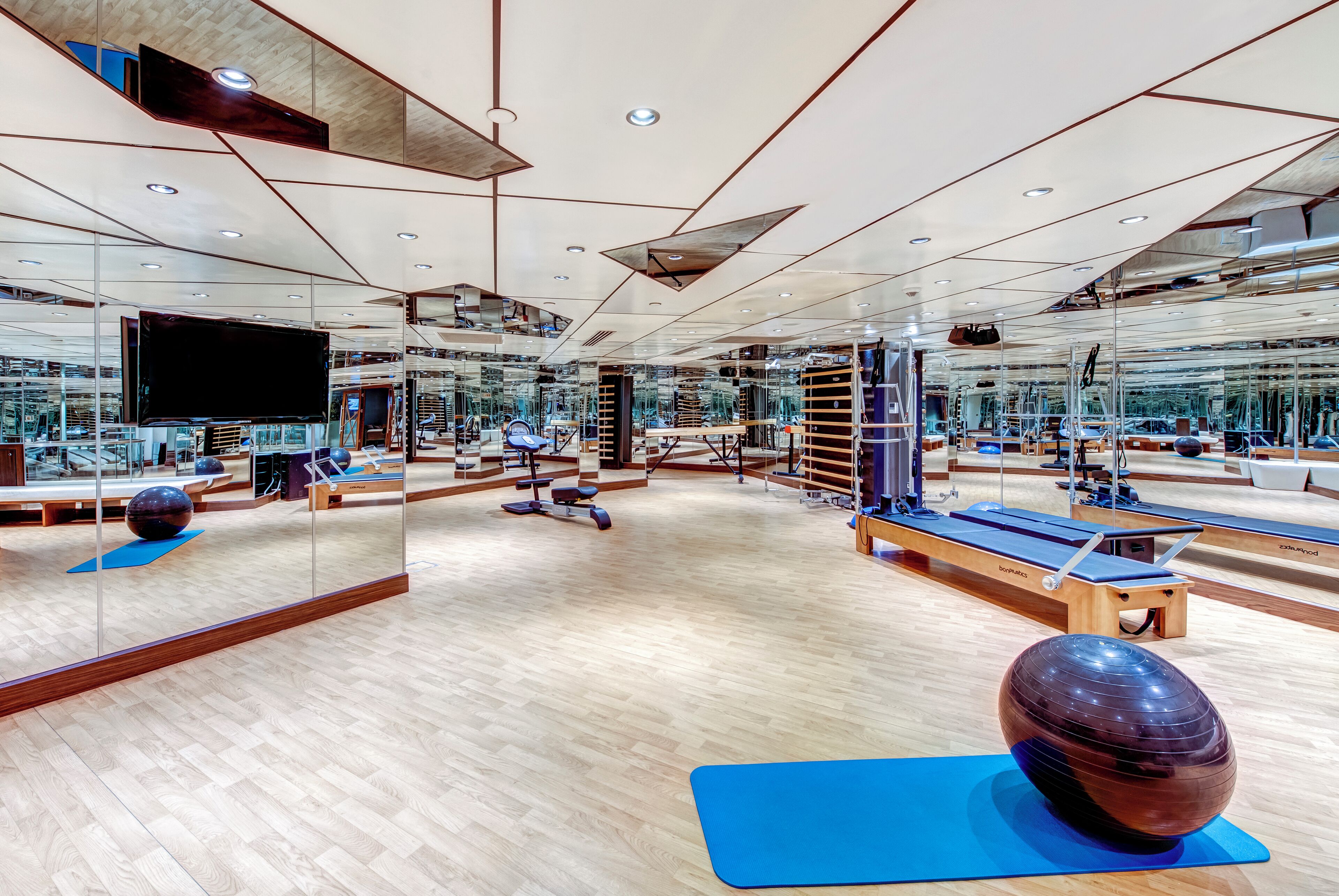 A modern gym with mirrored walls, wooden flooring, and various exercise equipment.