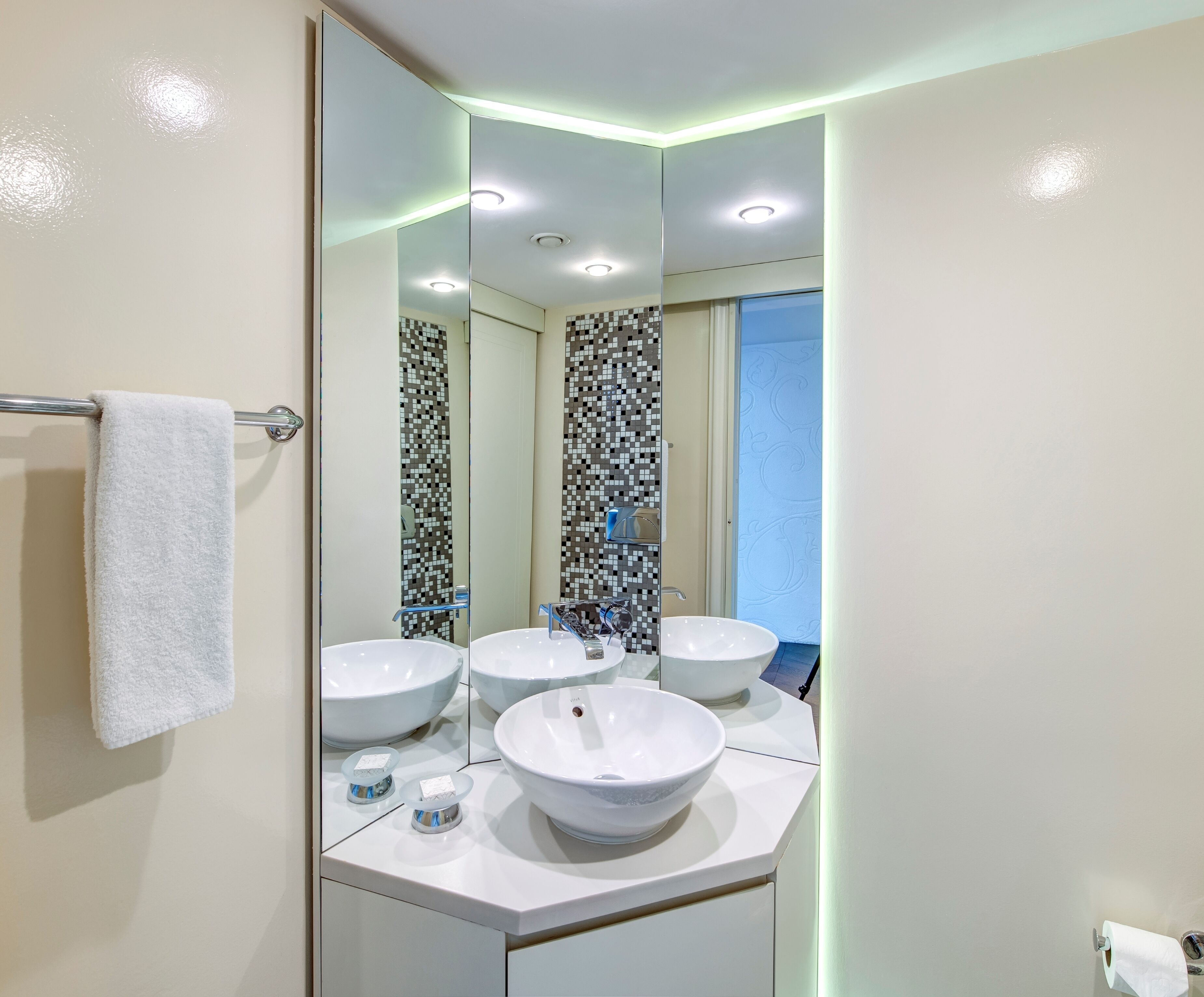 A bathroom with three white sinks, a towel rack, and a mirror reflecting the room.