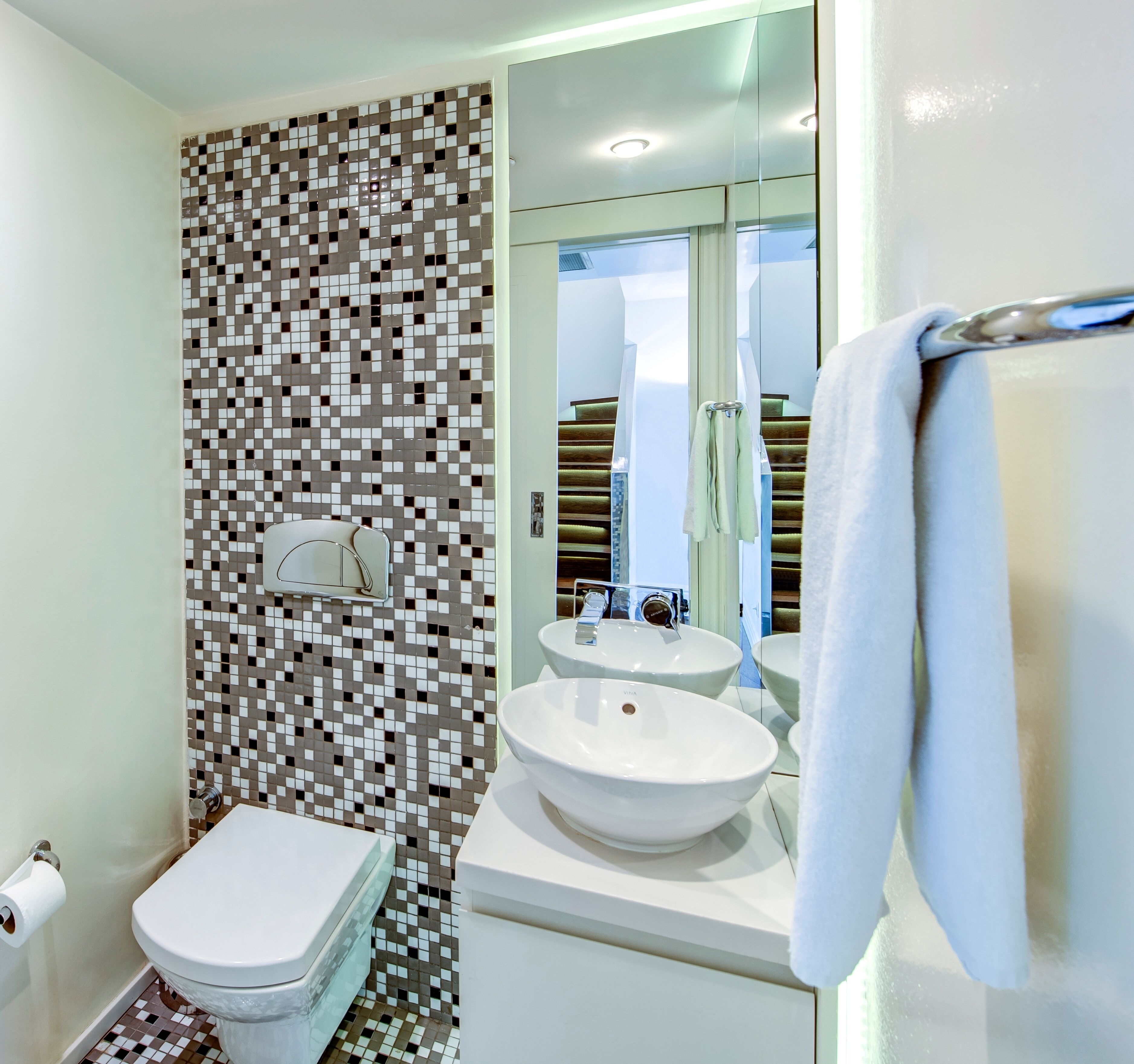 A modern bathroom with a mosaic tile wall, a toilet, a sink, and a towel rack.