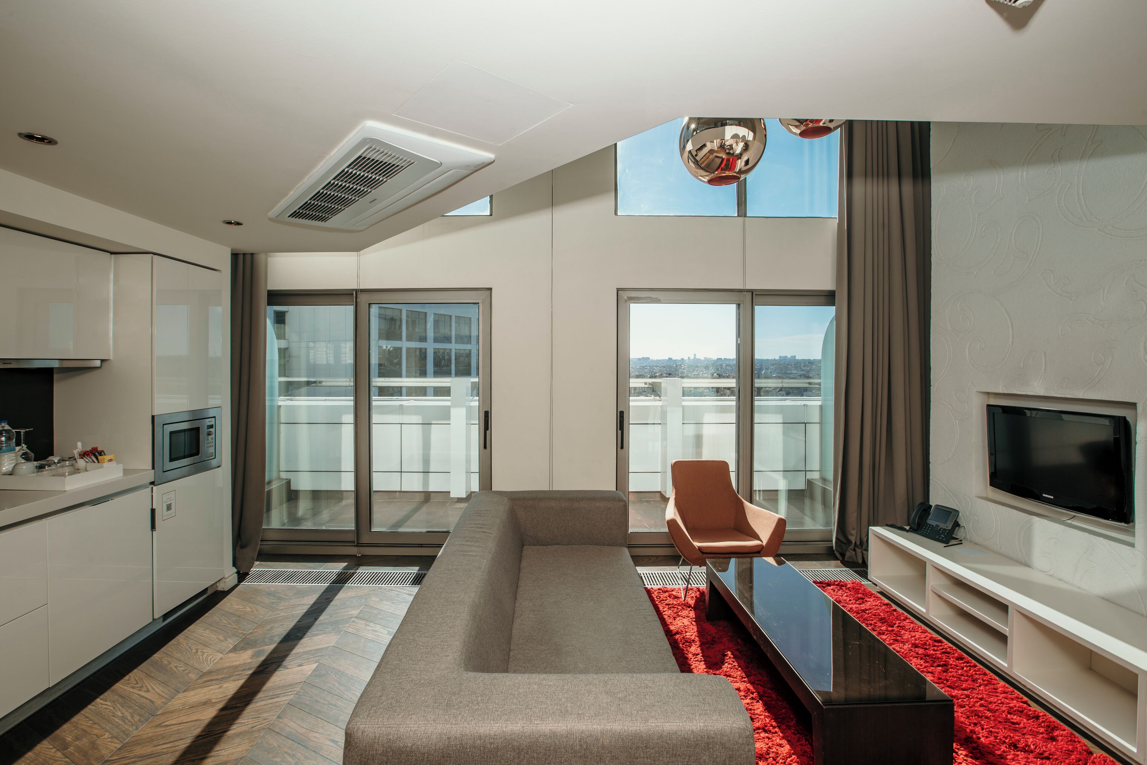 A modern living room with a sofa, a red rug, a flat-screen TV, and a city view through large windows.