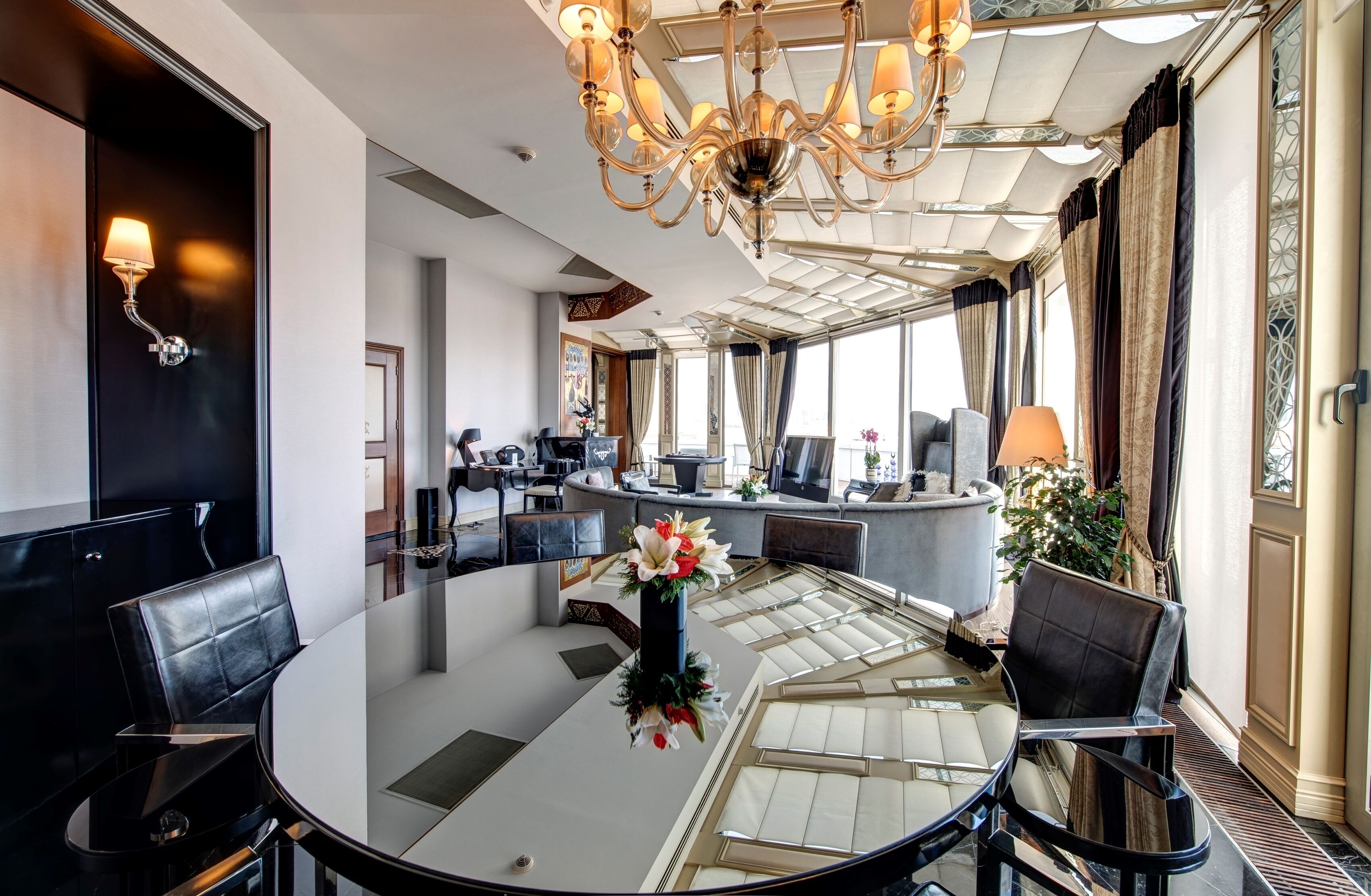 A modern hotel lobby with a round table, leather chairs, a chandelier, and a reception desk.