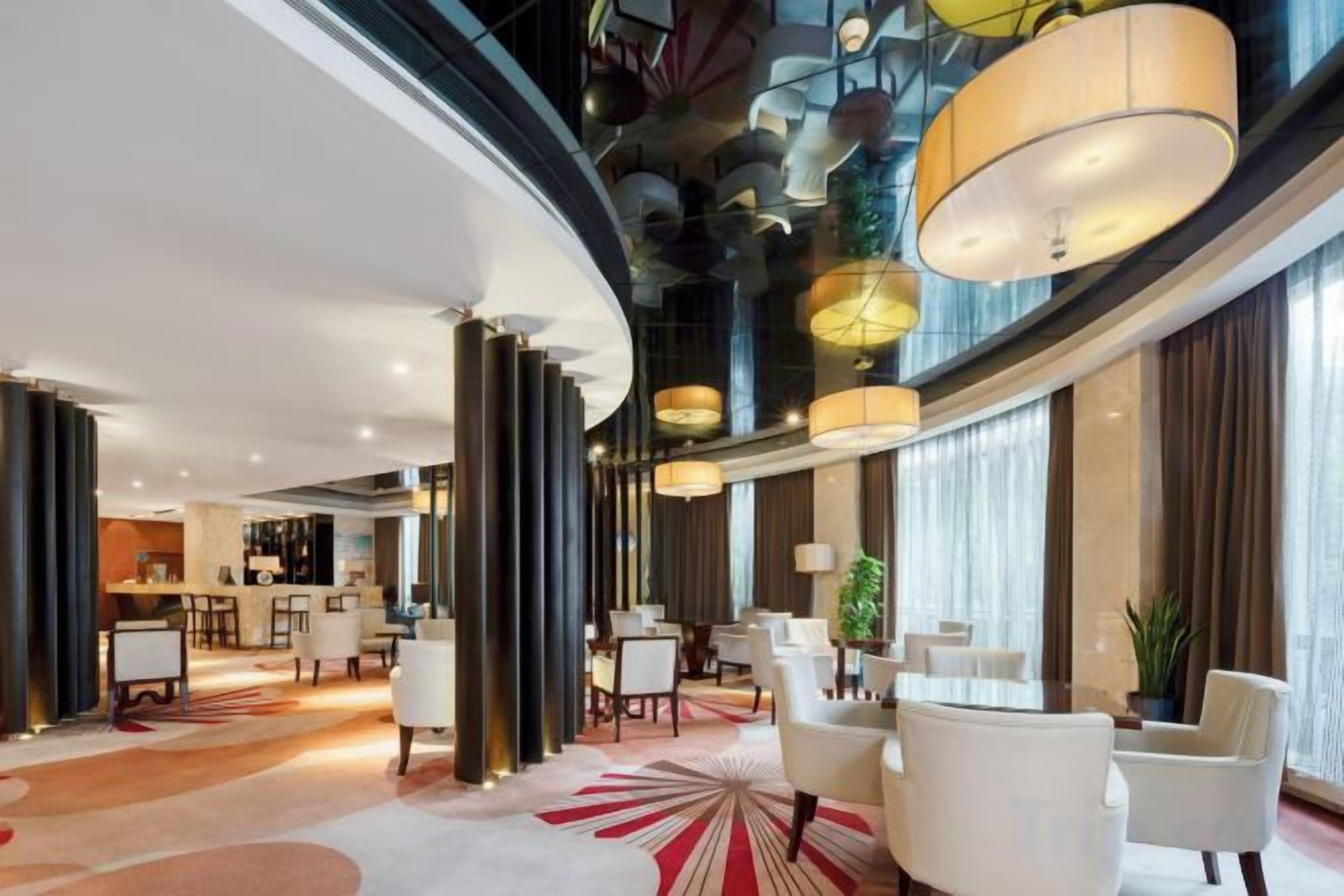 Un moderno vestíbulo de hotel con techo curvo, ventanas amplias y una zona de estar central con sillas blancas.