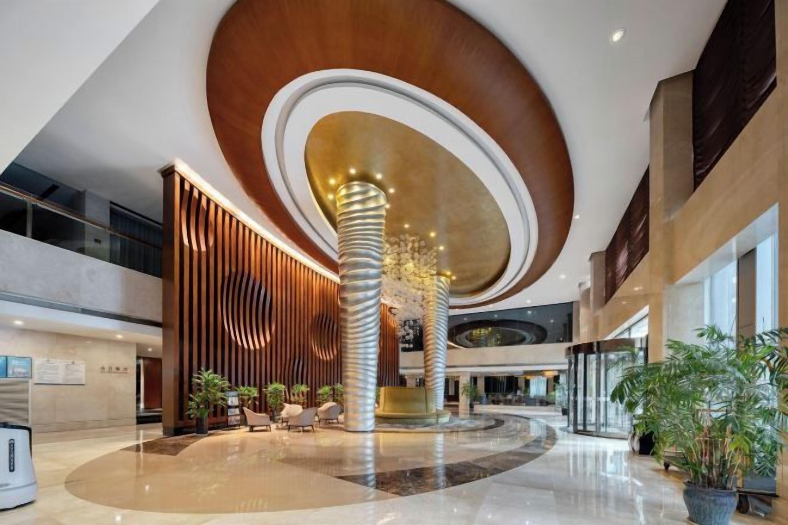 A spacious lobby with a central column, seating area, and potted plants.