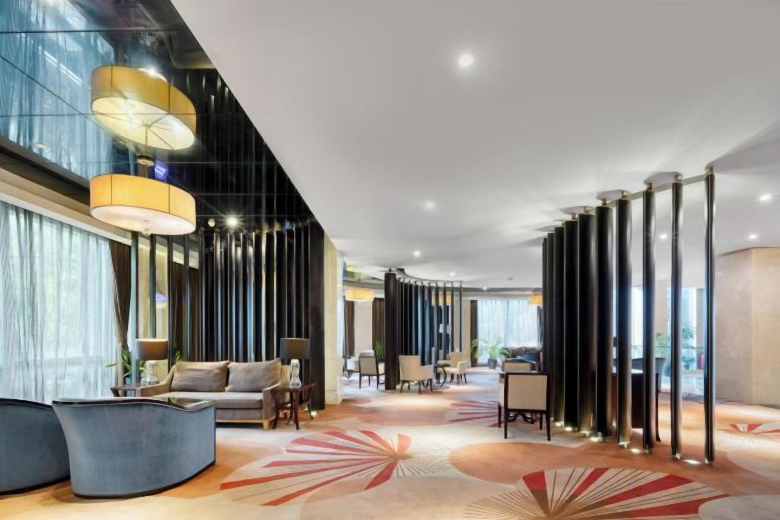 Un moderno vestíbulo de hotel con un sofá curvo, una mesa de centro, un tapiz con diseño geométrico y altas columnas cilíndricas.
