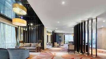 Un moderno vestíbulo de hotel con un sofá curvo, una mesa de centro, un tapiz con diseño geométrico y altas columnas cilíndricas.