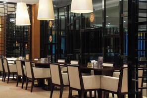 A dining area with tables and chairs, large windows, and hanging light fixtures. - East Harbour Hotel (Ningbo)
