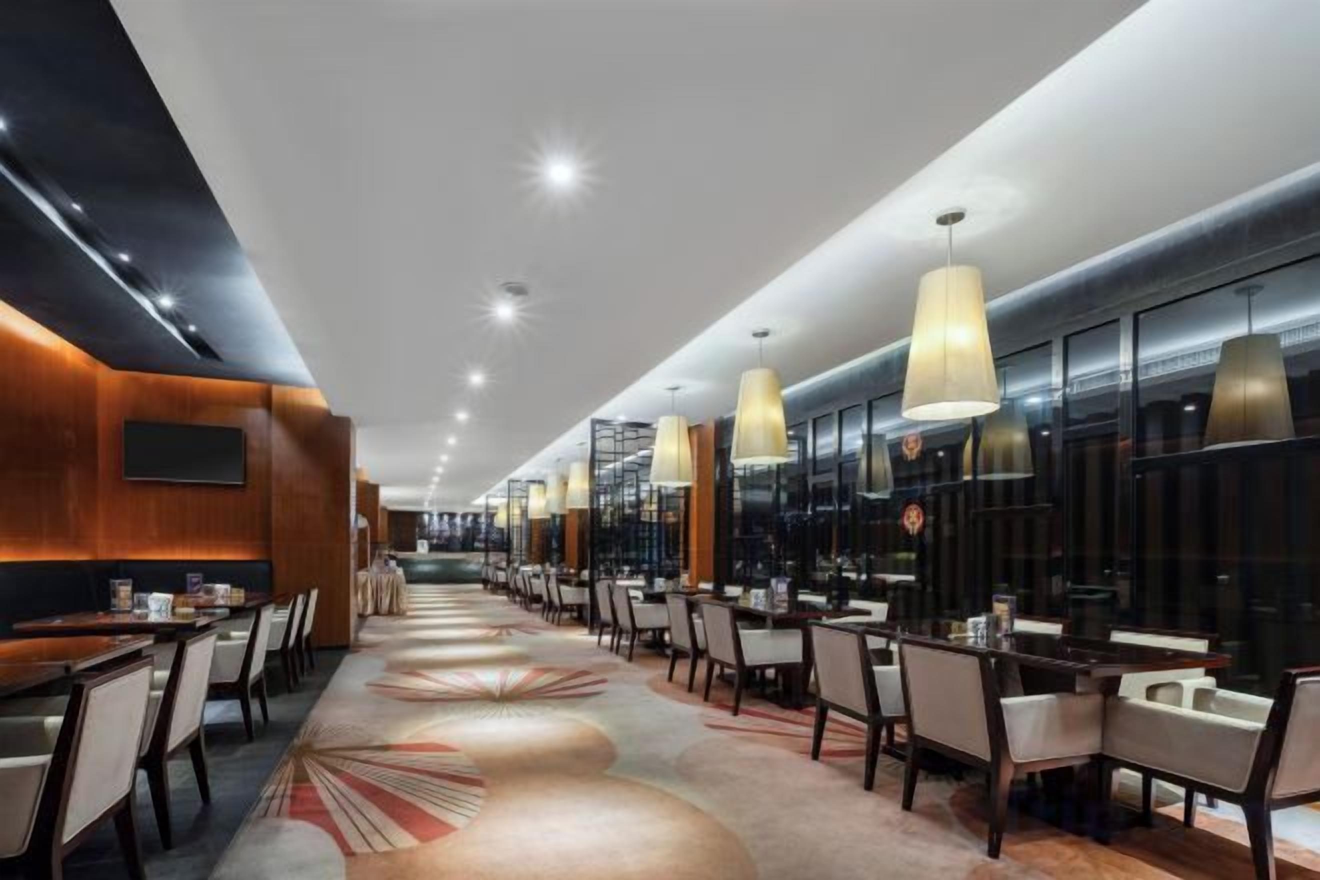 A modern hotel lobby with a long reception desk, multiple seating areas, and pendant lighting.