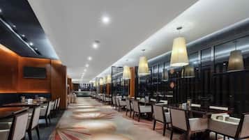 A modern hotel lobby with a long reception desk, multiple seating areas, and pendant lighting.