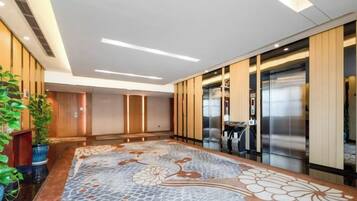 Eine Hotelhalle mit einem gemusterten Boden, Aufzügen und einem Empfangsbereich.