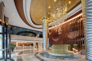 A spacious lobby with a central seating area, a reception desk, and a modern chandelier.