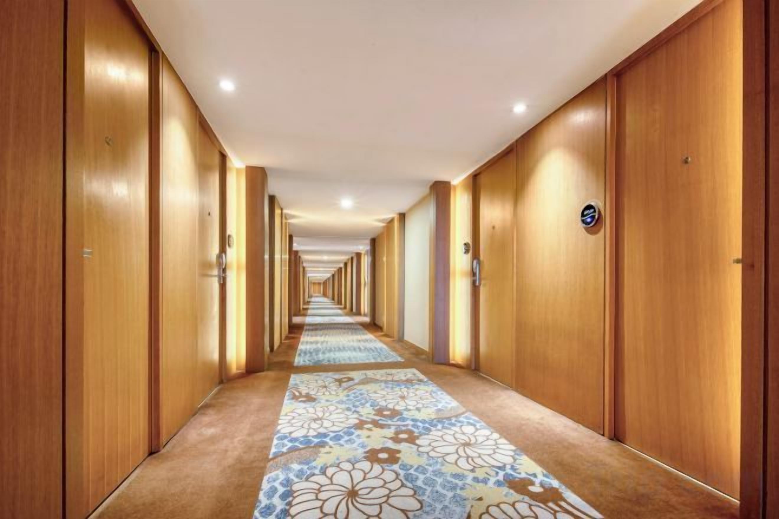 A hotel hallway with wooden doors, a patterned carpet, and a sign indicating the direction to the elevator.