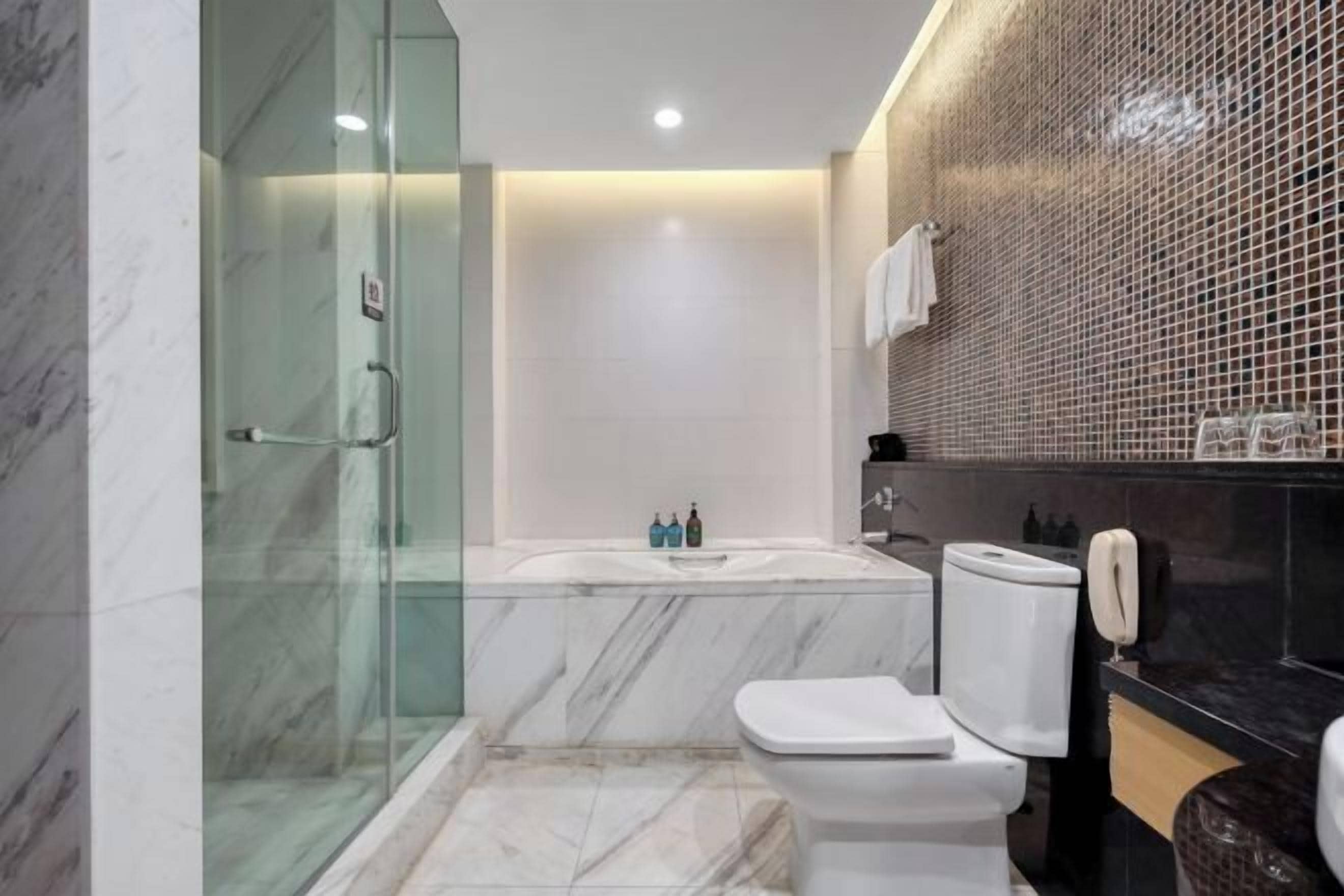 Un baño moderno con ducha envuelta en vidrio, inodoro blanco, bañera y pared con azulejos negros.