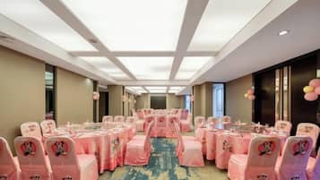 A banquet hall with rows of tables and chairs, a carpeted floor, and a ceiling with recessed lighting.