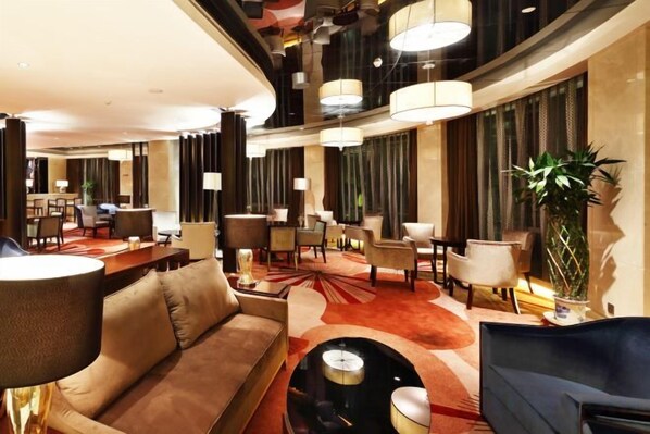 A hotel lobby with a central seating area, multiple tables, and a large plant.