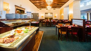 Zona de bufé con diversas opciones de comida, un candelabro y varias mesas y sillas para comer.