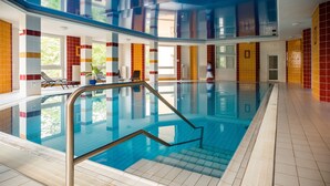 Una piscina interior con paredes de vidrio transparente, suelo de baldosas y escalera metálica.