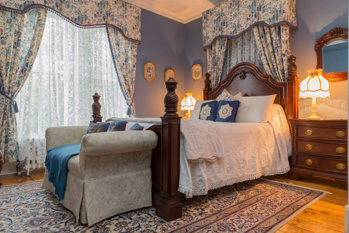 Un dormitorio con cama con dosel, una mesita de noche de madera, un aparador y una silla.