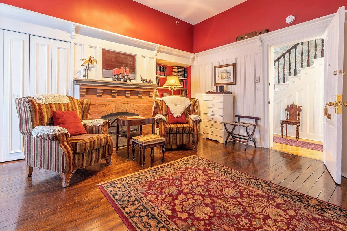 Una sala de estar acogedora con chimenea, sillones a rayas, un tapete estampado y una estantería.