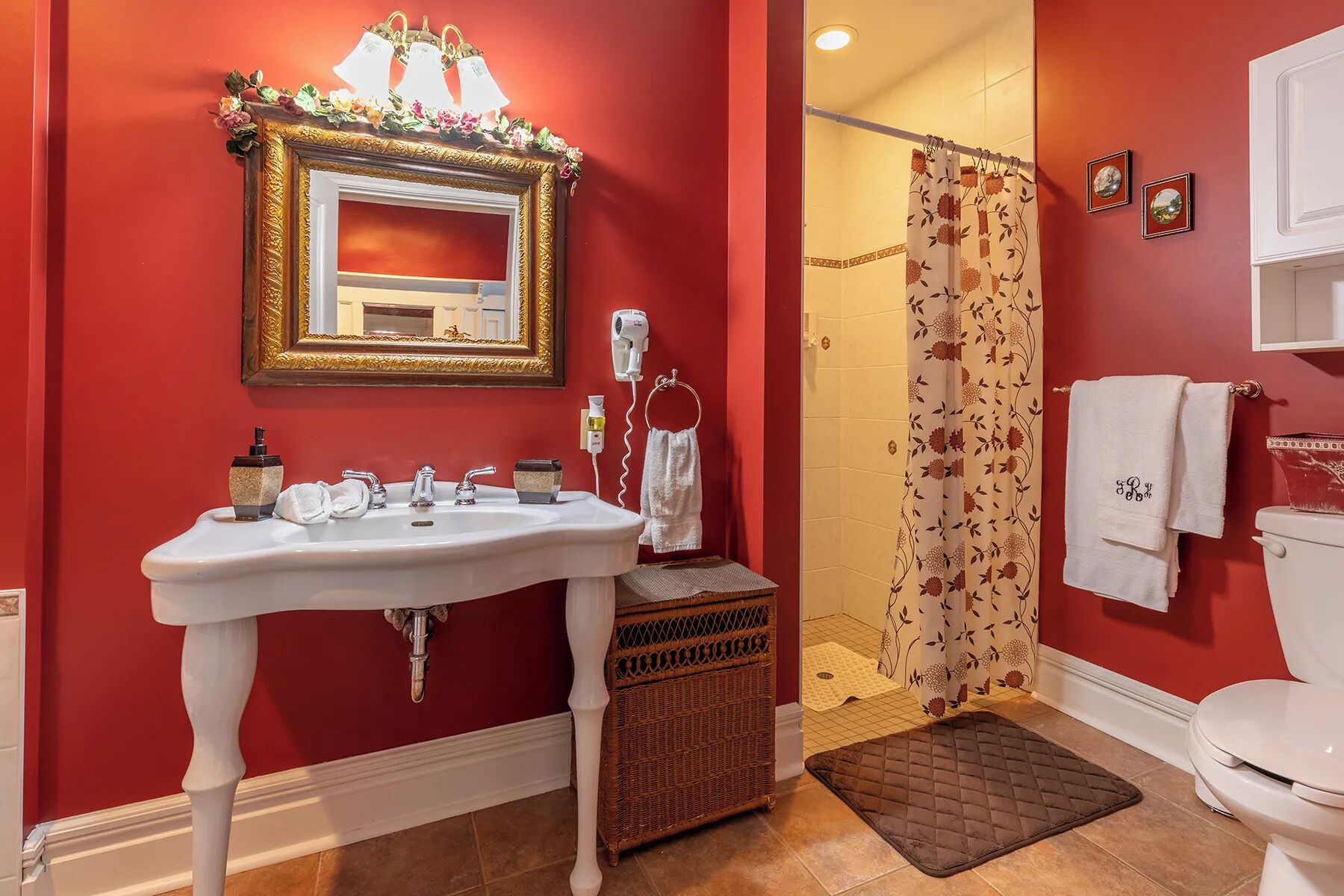 A bathroom with a white sink, a mirror with a gold frame, a shower curtain with a floral pattern, and a white toilet.