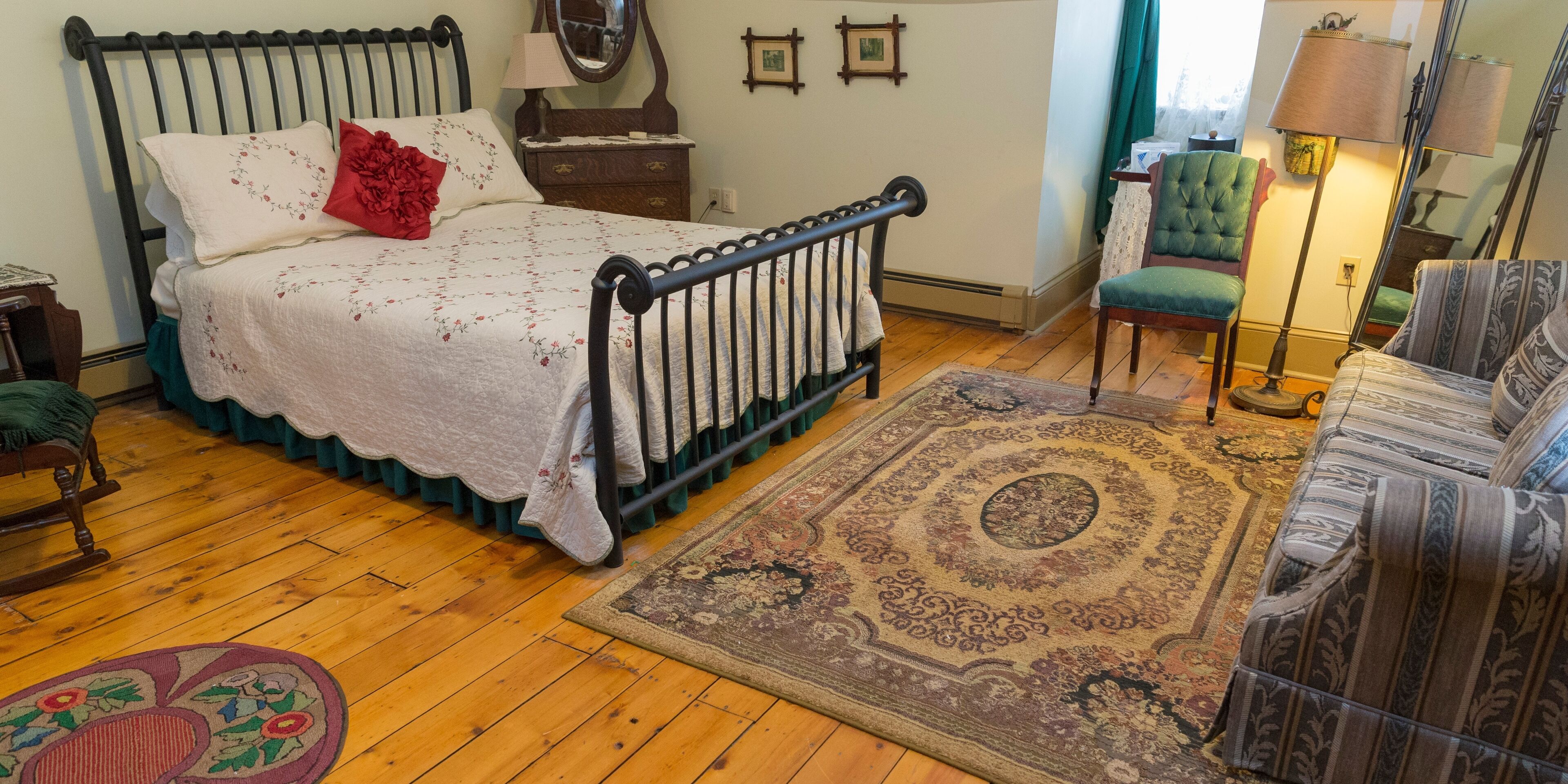 A bedroom with a bed, a green armchair, a patterned rug, and a wooden floor.