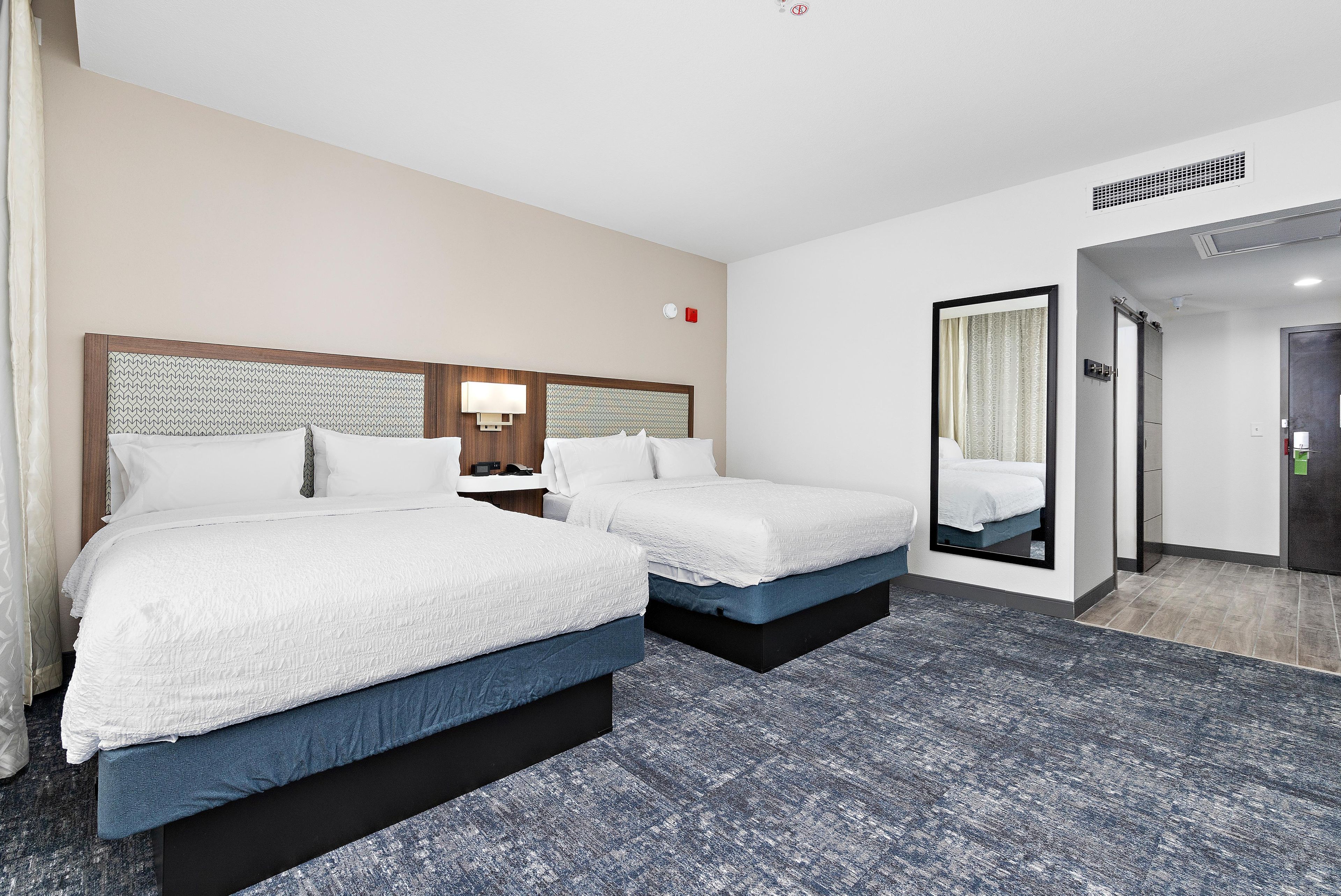 A hotel room with two beds, a large mirror, and a carpeted floor.