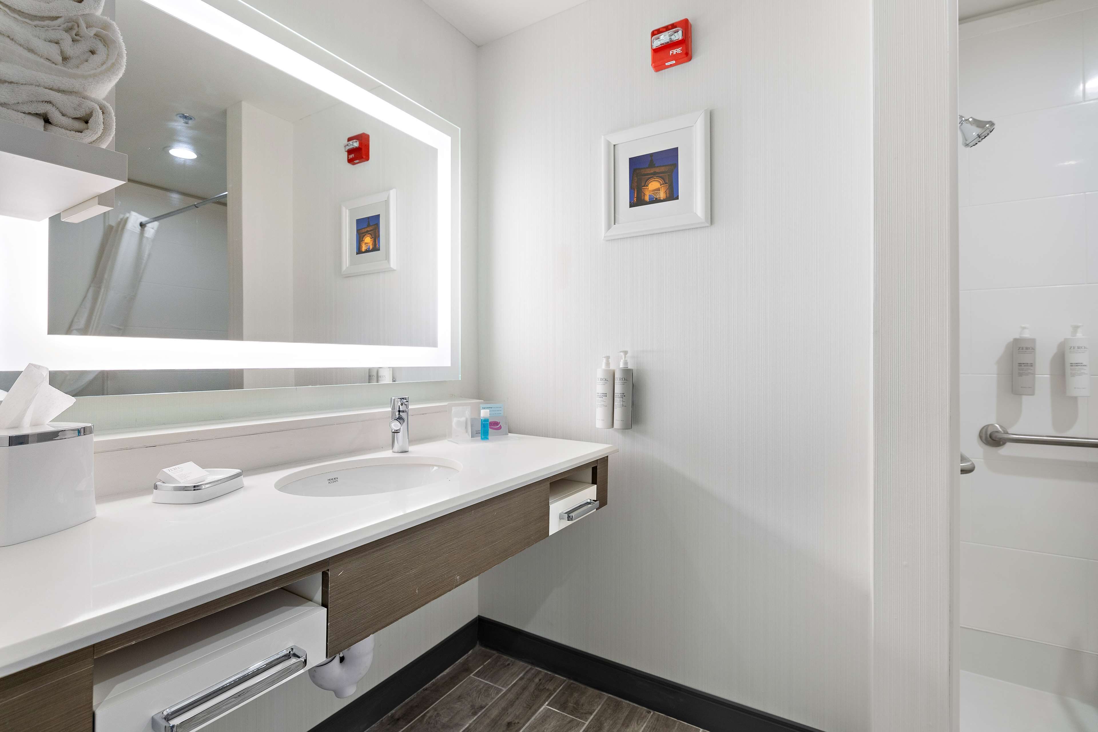 A modern bathroom with a white sink, a large mirror, a towel rack, and a shower area.