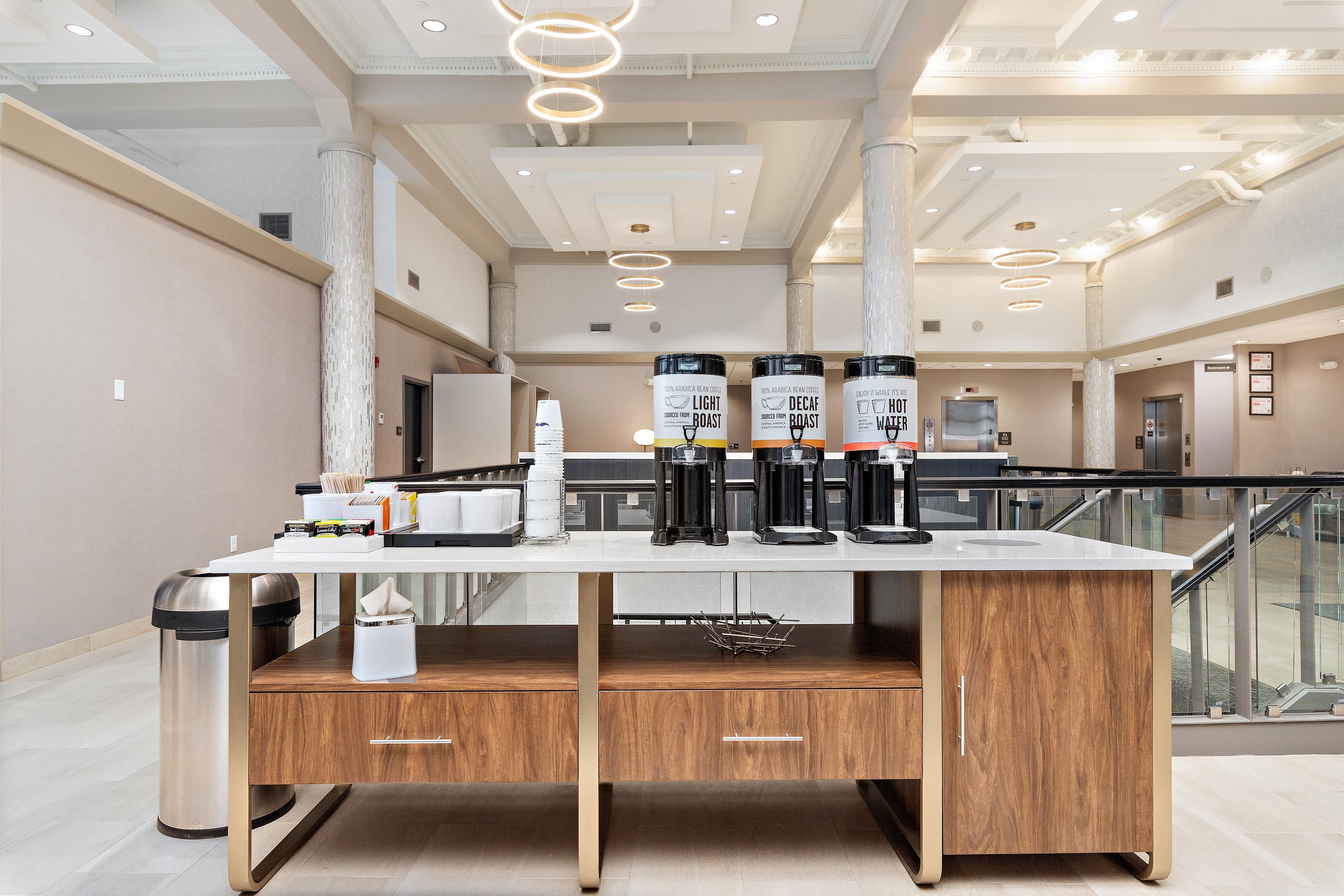 A modern hotel lobby with a coffee station, a trash bin, and a staircase.