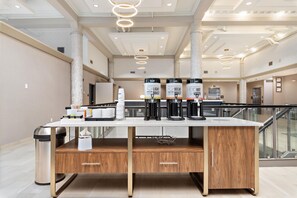 A modern hotel lobby with a coffee station, a trash bin, and a staircase. - Hampton Inn Kansas City/Downtown Financial District (Kansas City)
