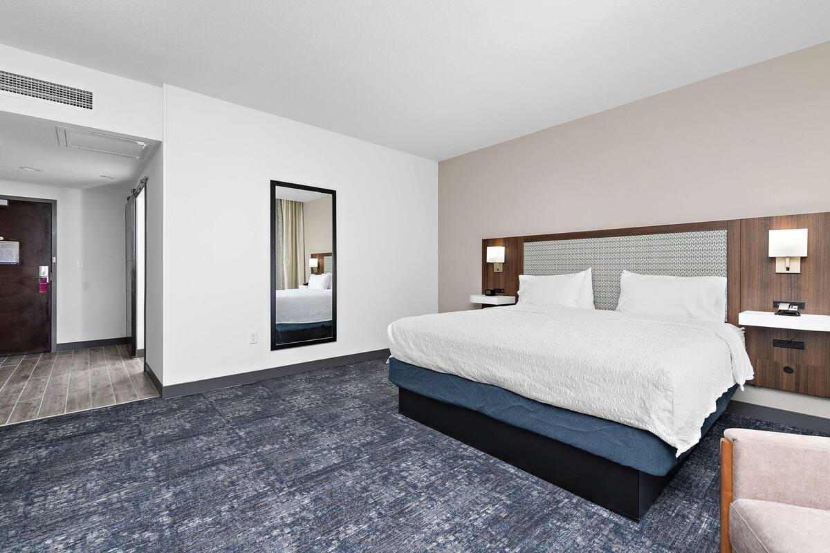 Une chambre d’hôtel moderne avec un grand lit, un miroir, une table de chevet et une lampe fixée au mur.
