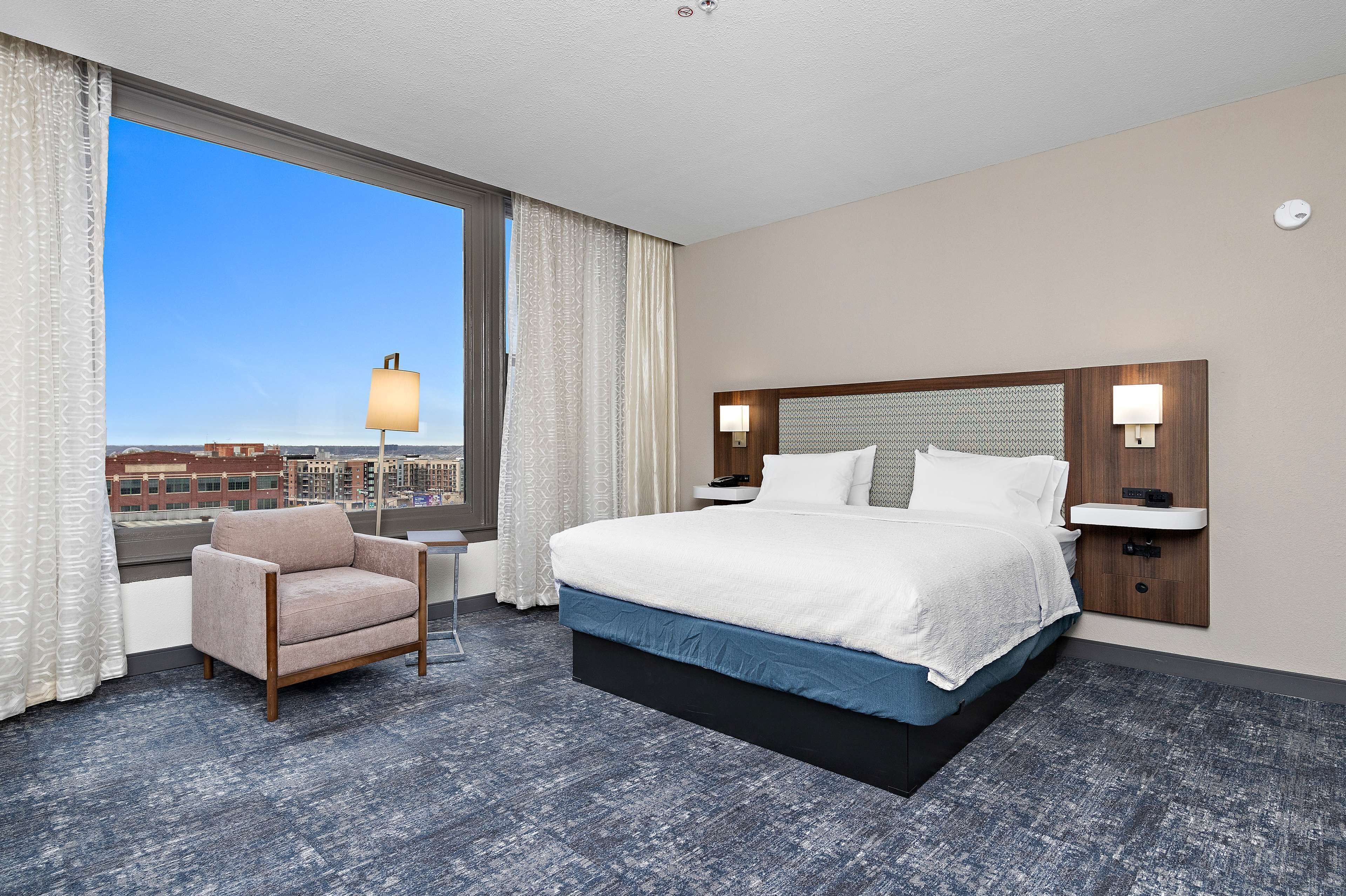 Une chambre d’hôtel avec un grand lit, une chaise, une table de chevet et une vue sur la ville.
