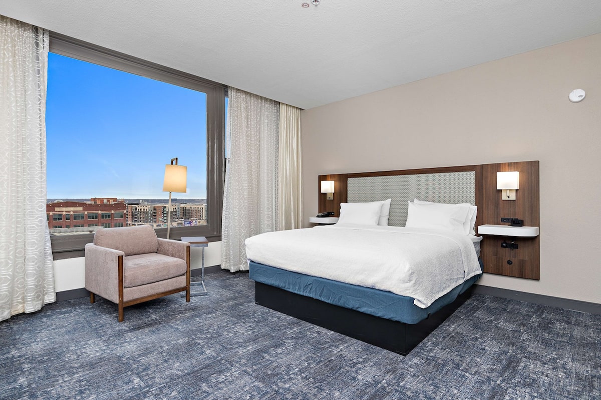 Une chambre d’hôtel avec un grand lit, une chaise, une table de chevet et une vue sur la ville.