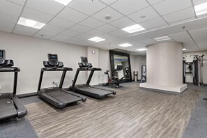 Een fitnessruimte met loopbanden, een hometrainer en een spiegel.