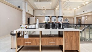 Um hall de hotel moderno com balcão de recepção, máquinas de café e uma lixeira.