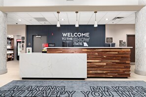 Een receptiehal van een hotel met een modern design, met een marmeren receptiebalie, een welkomstbord en een digitaal scherm.