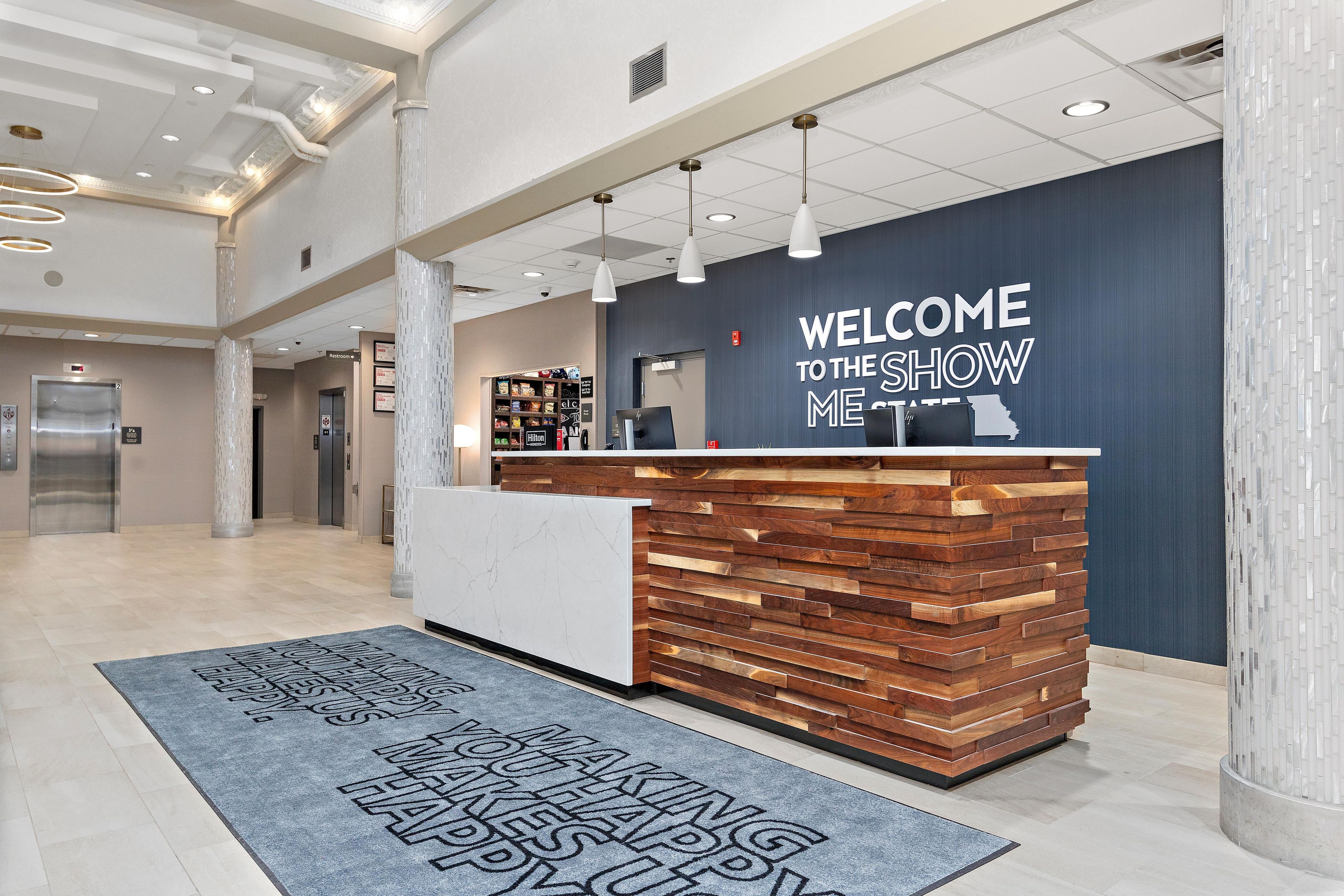 A reception area with a modern design, featuring a wooden reception desk, a welcome sign, and a digital display.