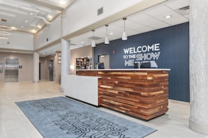 A reception area with a modern design, featuring a wooden reception desk, a welcome sign, and a digital display. - Hampton Inn Kansas City/Downtown Financial District (Kansas City)