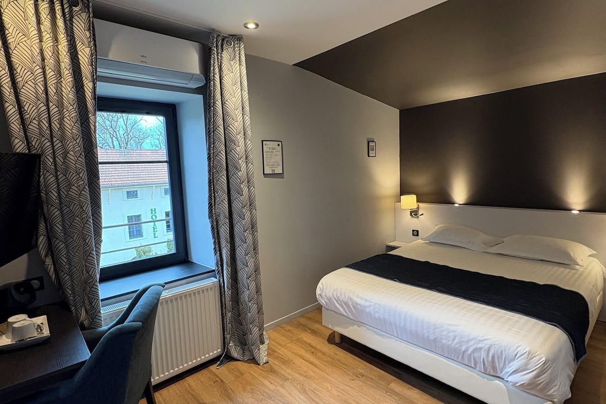 A modern hotel room with a bed, a desk, and a window with curtains.