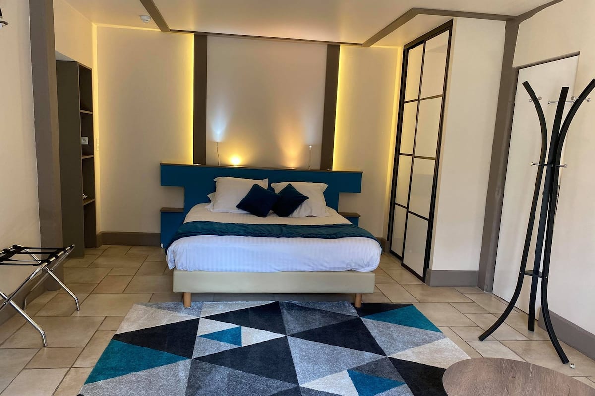 A modern bedroom with a bed, geometric-patterned rug, and a standing lamp.