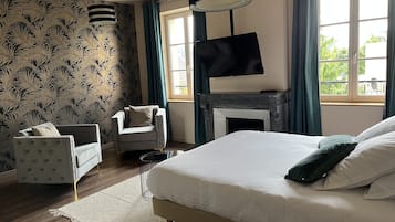 Une chambre à coucher avec un lit, un téléviseur fixé au-dessus d’une cheminée, un fauteuil et un papier peint à motifs.