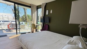 A hotel room with a large bed, a desk with a chair, a TV, and a view of the outdoors. - Hôtel de la Vinaigrerie (Joinville)