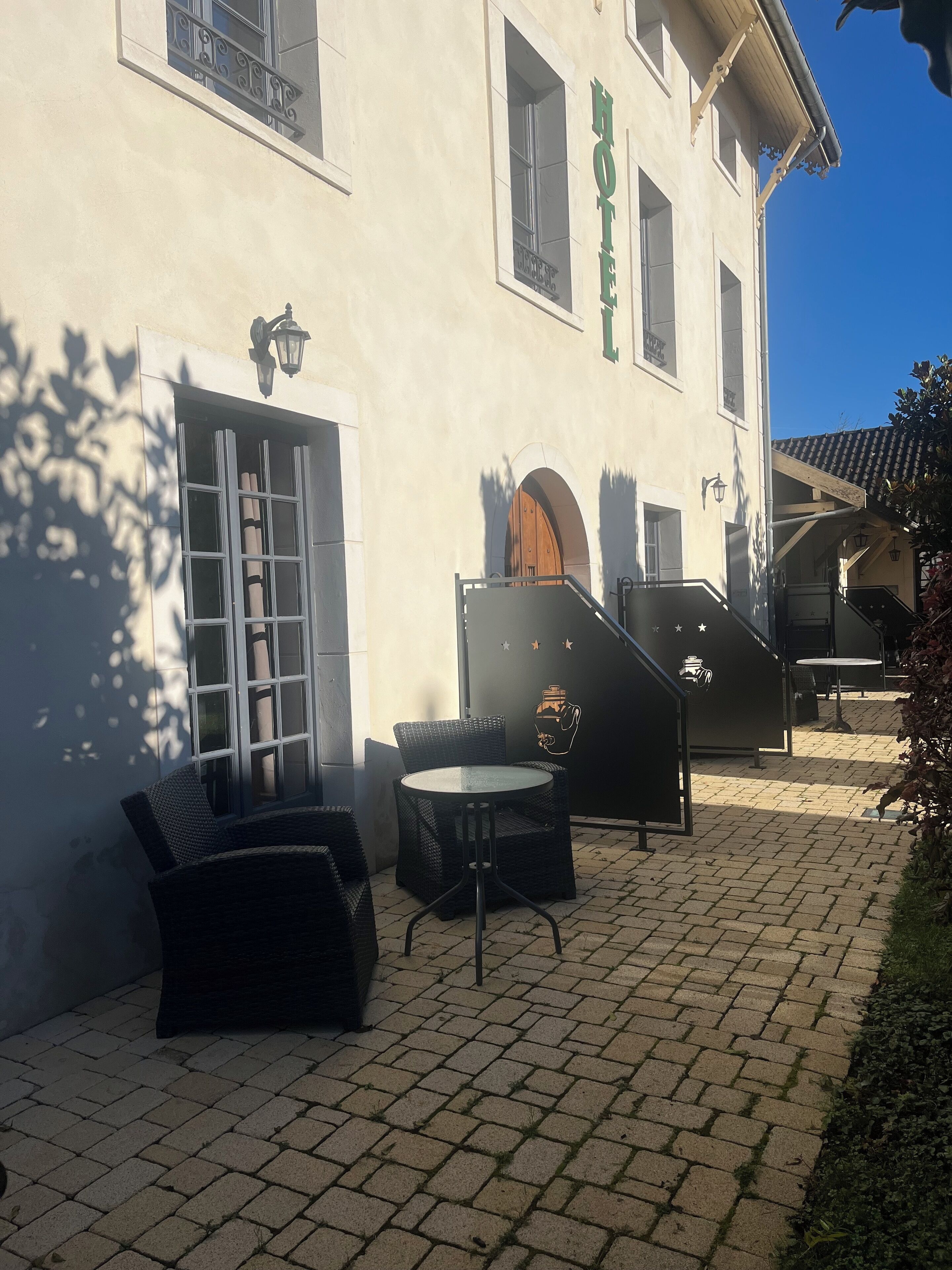 A hotel exterior with a paved patio, wicker furniture, and a staircase leading to the entrance.