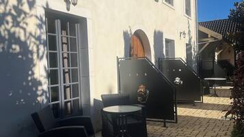 A hotel exterior with a paved patio, wicker furniture, and a staircase leading to the entrance.