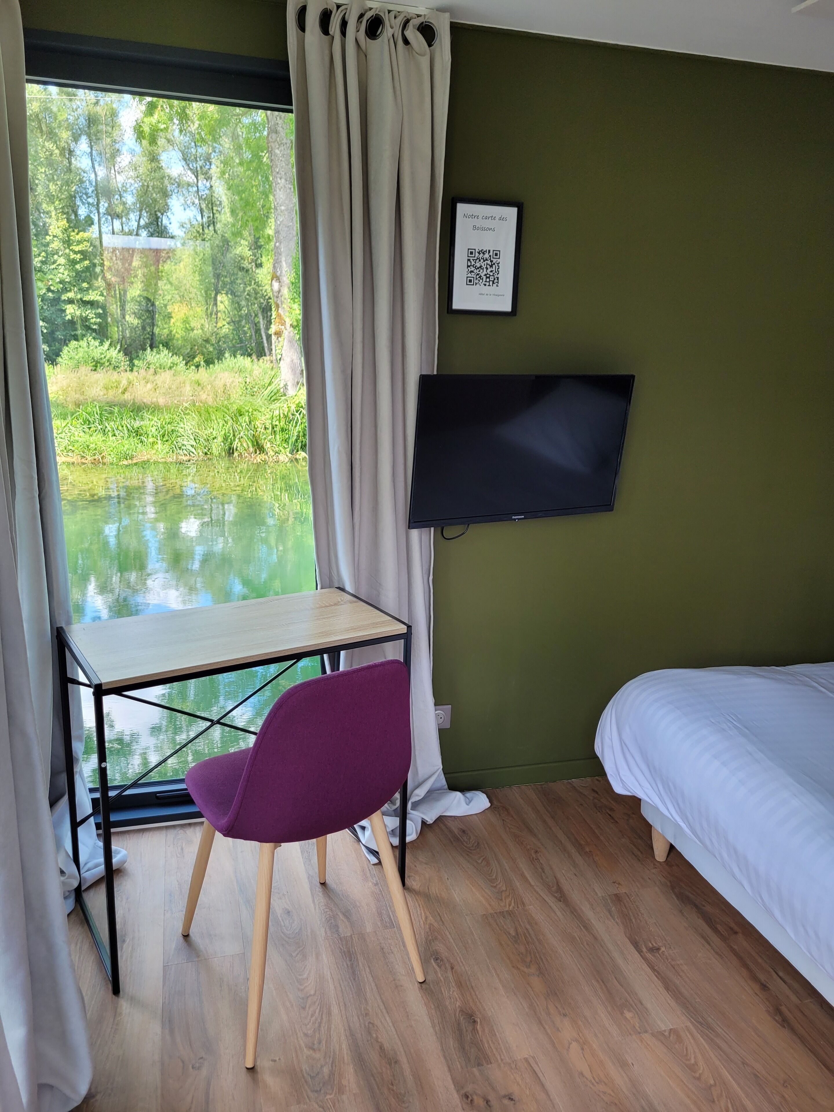 A room with a bed, a desk with a chair, a TV mounted on the wall, and a window with curtains.