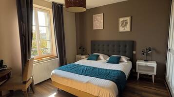 A bedroom with a large bed, a desk, and a chair. There is a window with curtains, a radiator, and a ceiling light fixture.