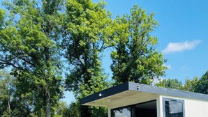 A modern houseboat with a glass door, a small deck, and a view of the surrounding greenery. - Hôtel de la Vinaigrerie (Joinville)